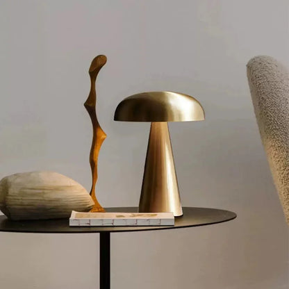 Gold table lamp on a round black surface with abstract sculpture and textured vase against a neutral background
