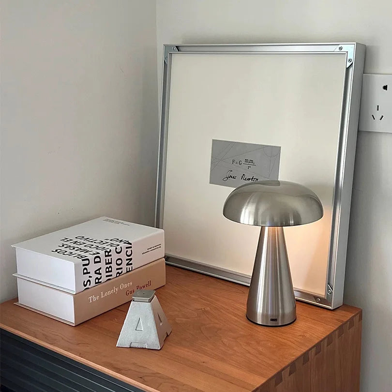 Silver lamp on a wooden surface with books and a framed picture in the background.